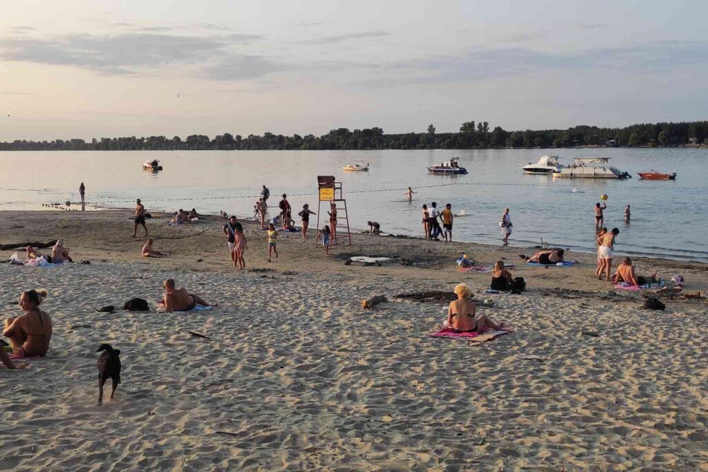 People relaxing and swimming at Lido Beach on Great War Island near Zemun, Serbia, with boats anchored in the Danube.