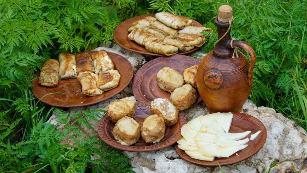 Traditional Serbian breakfast served outdoors: pancakes, cheese, and meatballs on clay plates – showcasing rustic Balkan food culture