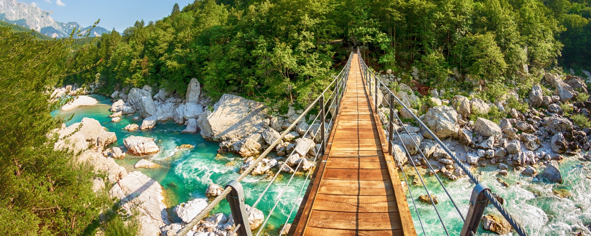 Wooden bridge and blue river sorrounded by forest and cliffs in Slovenia